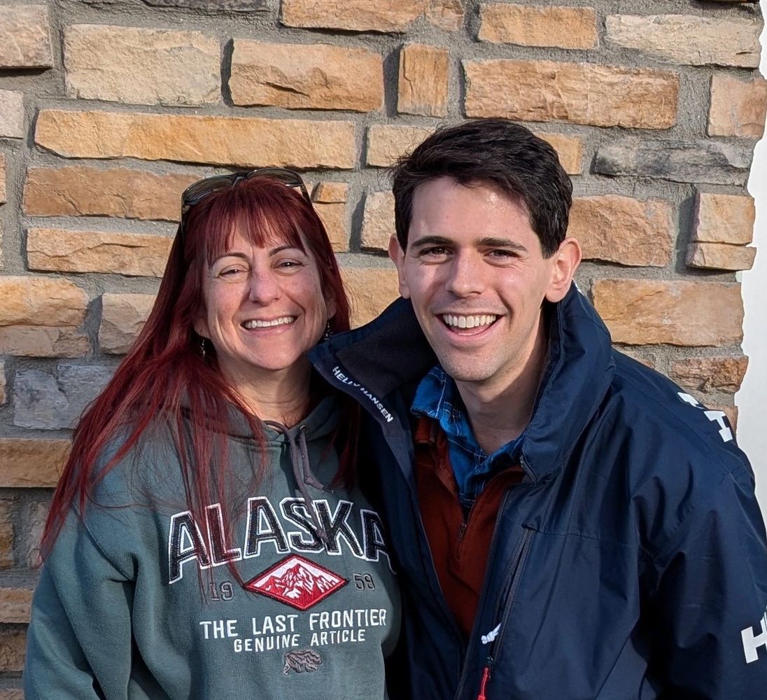 Smiling woman and man posing happily in front of a stone wall.