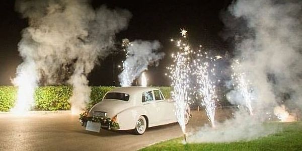 Classic white car surrounded by fireworks and smoke at night.