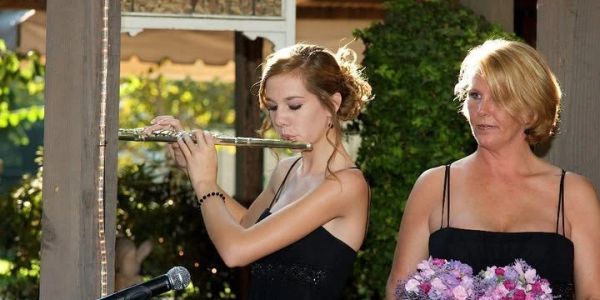 Young woman playing flute outdoors with another woman holding flowers.