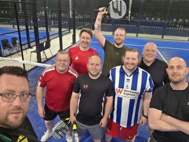 Group of men posing on a paddle tennis court.