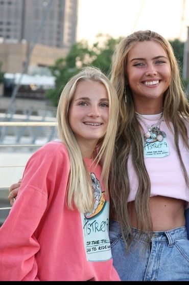 Two smiling young women posing outdoors in casual outfits with graphic tops.