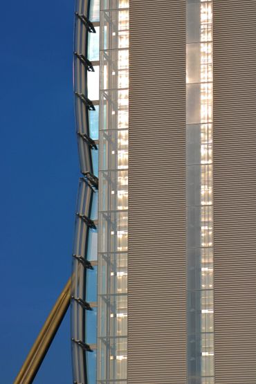 Close-up of a modern building facade with glass and metal panels illuminated by sunlight.