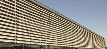 Modern building facade with horizontal sunshades under a clear sky.