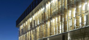 Modern building facade with illuminated vertical wooden panels at night.