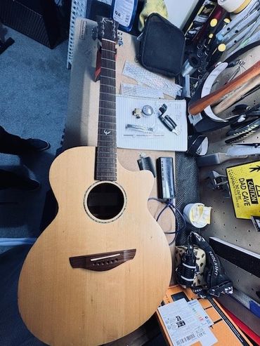 Acoustic guitar on a workbench surrounded by tools and notes.