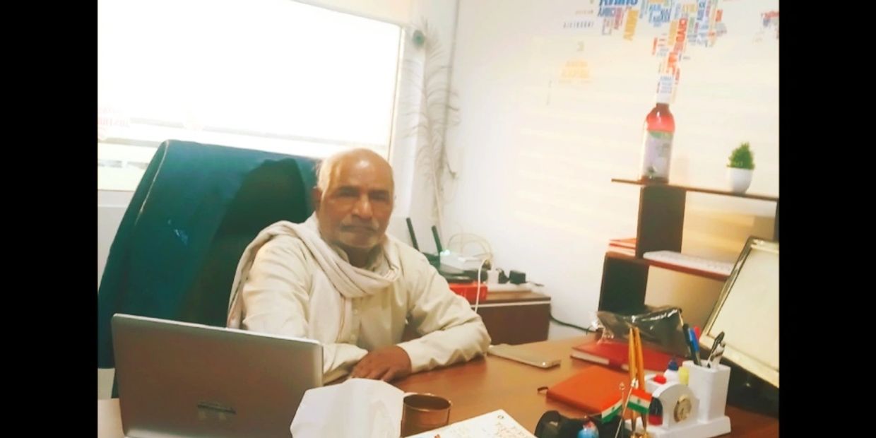 An elderly man sitting at a desk in a well-lit office space.