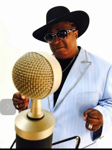 Man in stylish hat and sunglasses singing into a vintage microphone.