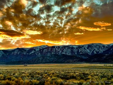 Dramatic golden sunset over snowy mountains with dramatic orange and blue clouds.