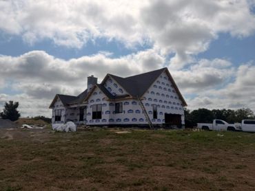 House under construction with wrap and a ladder leaning on it.
