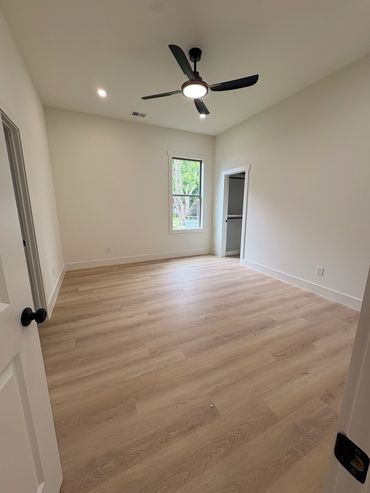 Empty room with light wood flooring and black ceiling fan.
