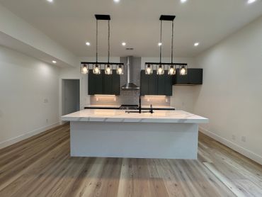 Modern kitchen with marble island and pendant lights.