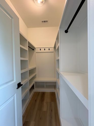 Empty white walk-in closet with shelving and wooden floor.