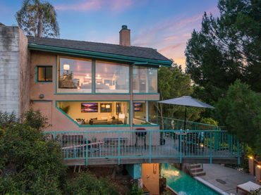 Modern house with large windows, a balcony, and a pool at sunset.