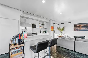 Modern kitchen and living room with white cabinetry and a gray sofa.