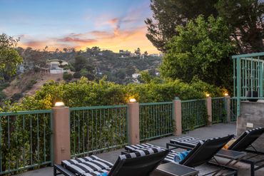 Sunset view from a patio with striped lounge chairs and green railing.