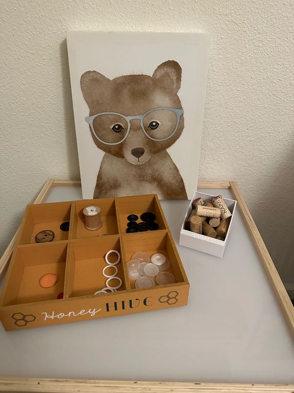 A light table with a picture of a bear and loose parts. Corks, buttons, thread spool.