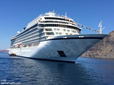 Large white cruise ship sailing in calm blue waters near rocky shores.