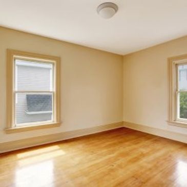 Empty room with wooden floor and two windows.