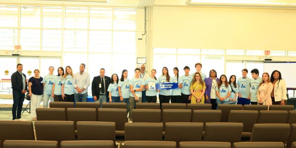 Group of young people and adults posing indoors, some wearing matching blue shirts.