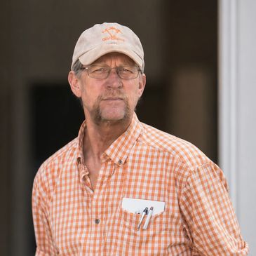 Man in a checked shirt and cap with pens in his pocket.