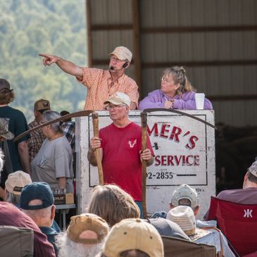 Auctioneer pointing while conducting an outdoor auction with attendees.