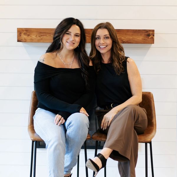 Two women sitting on chairs smiling at the camera.