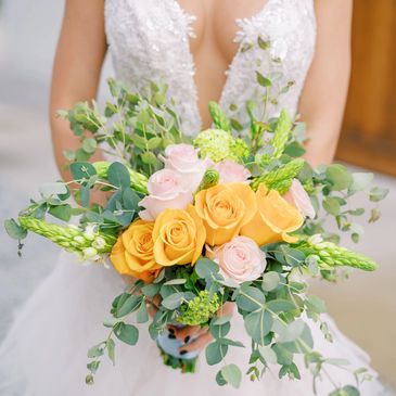 Bride holding a bouquet with yellow and pink roses.