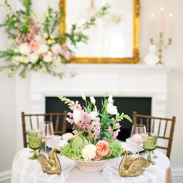 Elegant floral centerpiece on a white table with gold swan holders.
