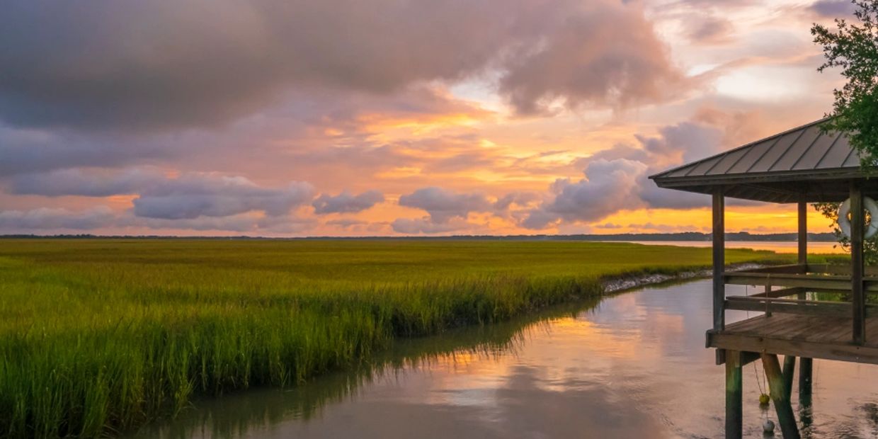 Sunset over marshland with a wooden dock shelter.