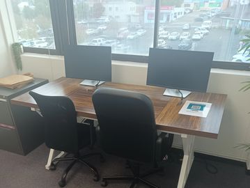 Office desk with two chairs and monitors by a window.