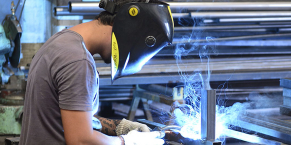 A welder wearing a protective helmet and gloves welding metal pieces.