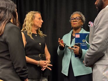 The Assemblymember speaks to a group of panelists in green and others in black and dark colors