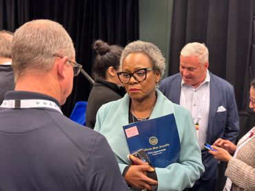Assemblymember holds an official folder while listening to a constituents story while other speak