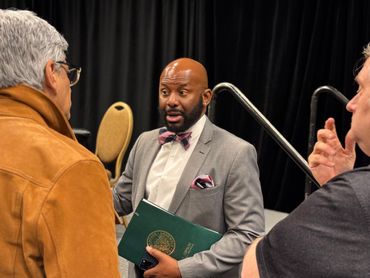The Assemblymember speaks animatedly holding an official folder in the audience after the event