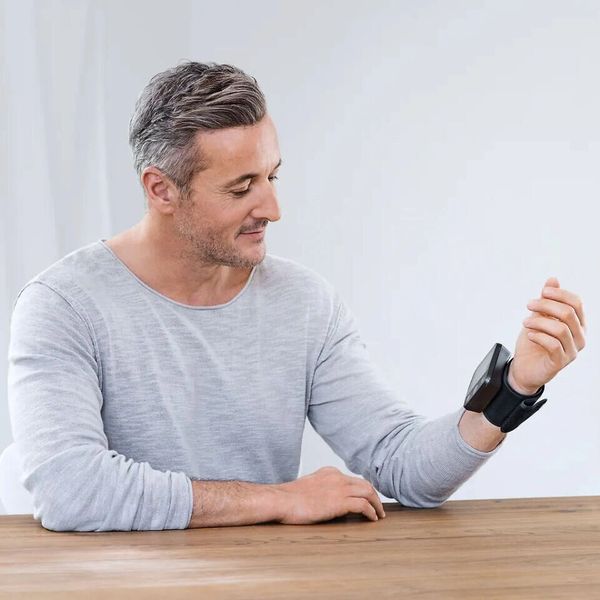 Man wearing a wrist blood pressure monitor while sitting at a table.
