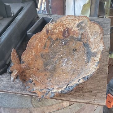 Rusty, scalloped metal bowl with a butterfly detail on a wooden barrel.
