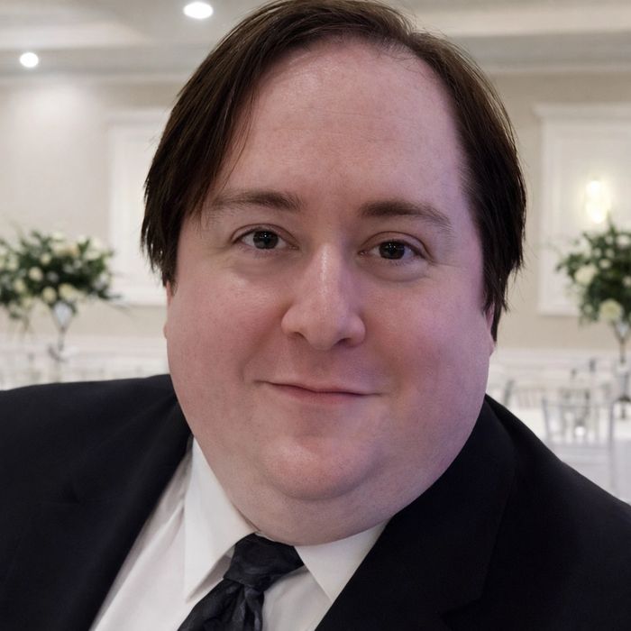 Smiling man in a suit at a formal event with floral decorations in the background.