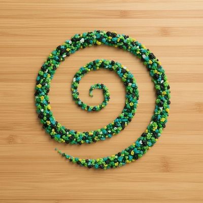 “Recycled foam particles arranged in a vibrant green and blue koru spiral on a natural bamboo background, symbolising sustainability, circular design, and Māori-inspired innovation.”