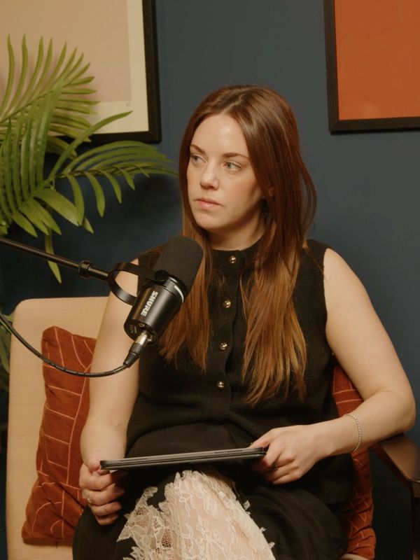 Woman with long brown hair speaking into a microphone while holding a tablet.