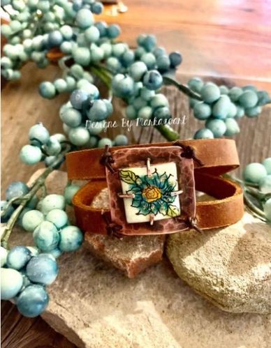 Enameled component has been hand torched and hand painted one of a kind design set atop leather str
