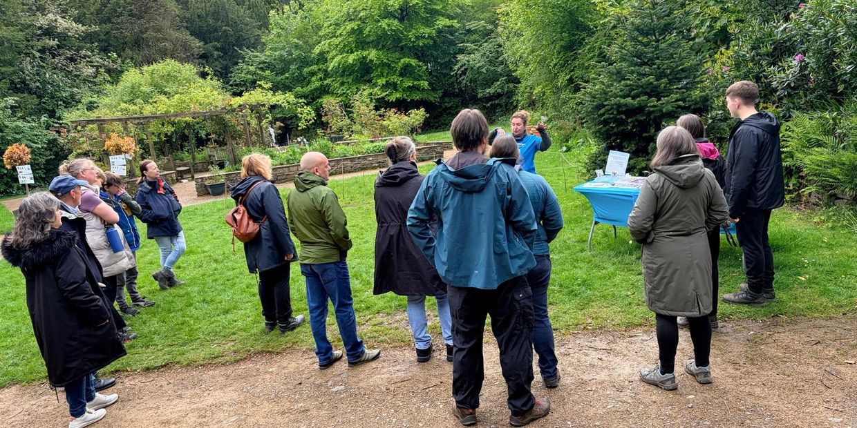 A group listens to a speaker in an outdoor garden setting.