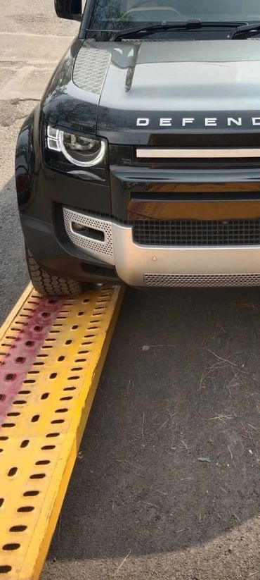 Front view of a black Land Rover Defender on a yellow ramp outside a service center.