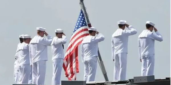 U.S. Navy sailors in white uniforms saluting the American flag.