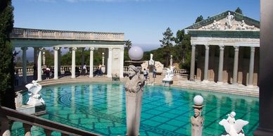 A classical-style outdoor pool with statues and columns under clear skies.