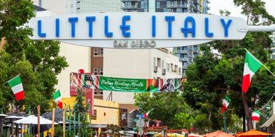 Entrance sign to Little Italy in San Diego with Italian flags and outdoor dining.