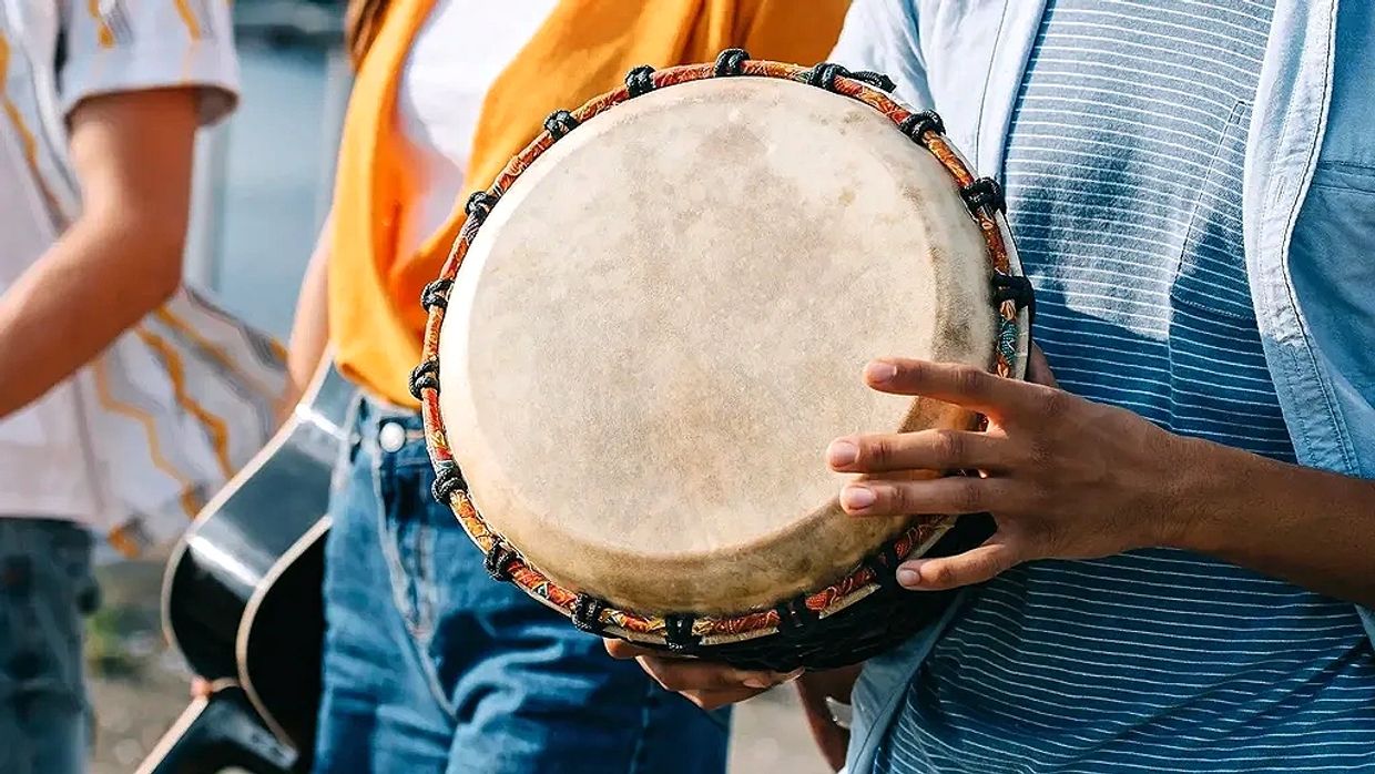 Person holding a traditional drum with others in the background.