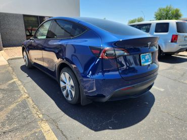 Blue Tesla Model Y parked in a sunny lot beside a white SUV.