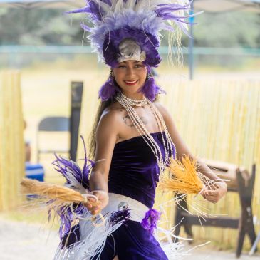 Woman in traditional Polynesian dance costume with purple feathers.