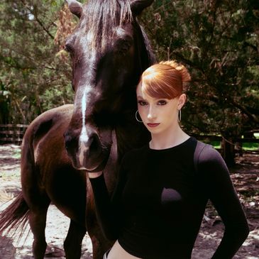 Woman posing with a black horse outdoors.