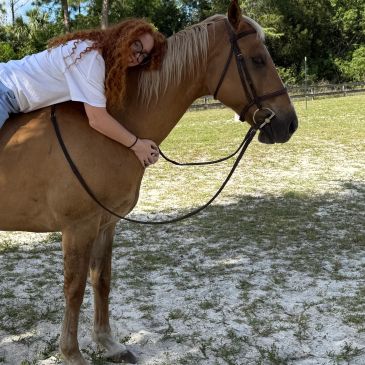 Person with red hair hugging a horse outdoors.
